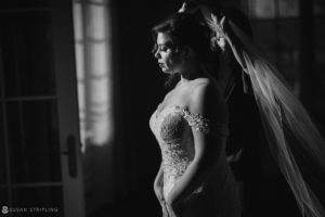 At Park Chateau, a bride is elegantly putting on her veil for her magical wedding day in a dimly lit room.