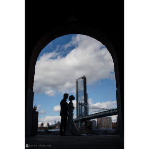 The wedding couple is silhouetted in front of the Brooklyn Bridge at Battery Gardens.