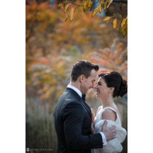 A wedding couple smiling in front of autumn leaves at Battery Gardens.