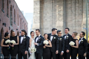 A group of bridesmaids and groomsmen in black tuxedos in front of Battery Gardens for a wedding.