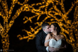 A bride and groom embrace in front of a tree at night during their wedding at Park Chateau.