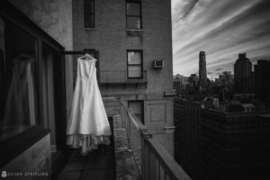 A black and white photo of a wedding dress hanging on a Manhattan balcony.