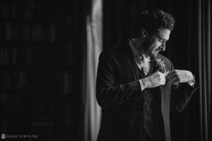 A black and white photo of a man adjusting his tie at a private club in Manhattan before attending a wedding.