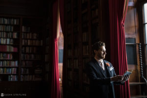 A man in a suit standing in front of a bookcase at a private club.