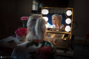 A woman is getting ready for her wedding, meticulously applying makeup in front of a mirror.