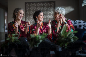 Three bridesmaids in robes sitting on a couch at a wedding.