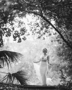 A wedding bride in a white dress walking through the woods of Quantum Leap Winery.