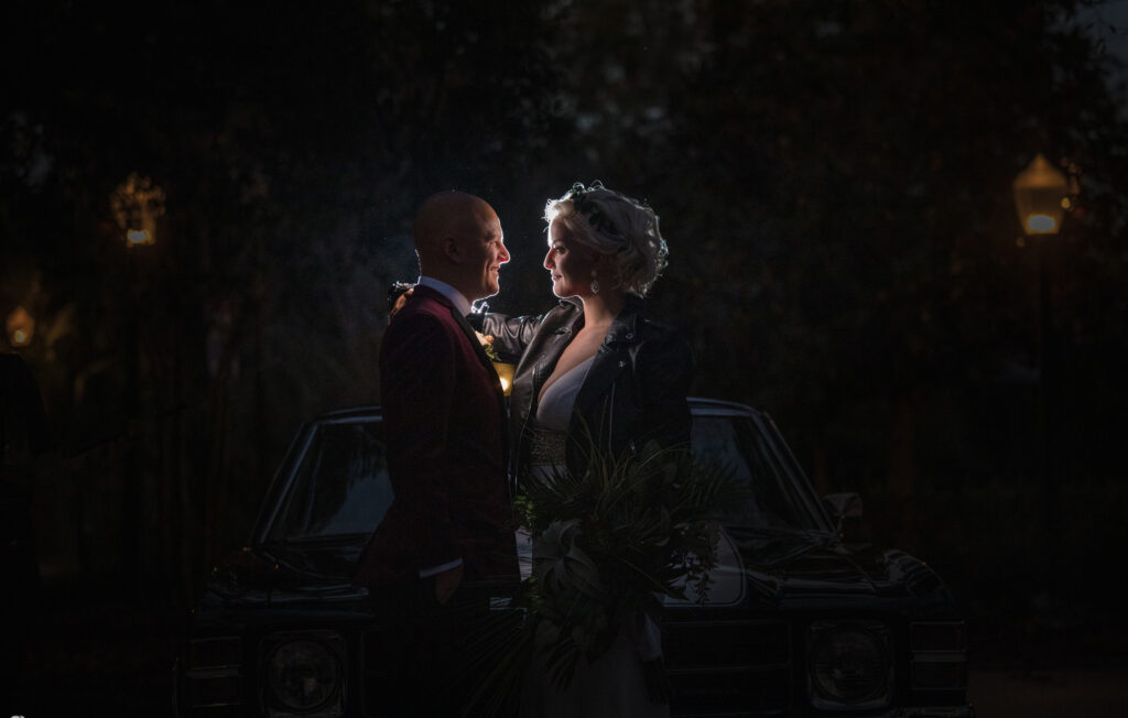 A wedding couple standing in front of a car at Quantum Leap Winery at night.