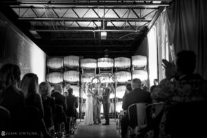 A wedding ceremony in the charming wine cellar of Quantum Leap Winery, captured beautifully in a black and white photograph.