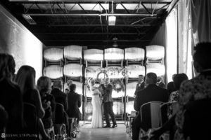 A bride and groom share a heartfelt kiss in front of wine barrels at their Quantum Leap Winery wedding.