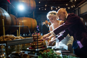 A wedding couple cutting a cake in front of wine barrels at Quantum Leap Winery.