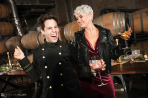A man and woman dressed in military uniforms standing next to wine barrels at their Quantum Leap Winery wedding.