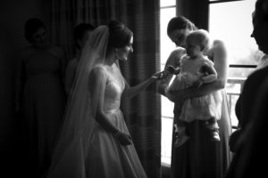 At the picturesque Alfond Inn, a radiant bride affectionately cradles a precious baby amidst her beaming bridesmaids.