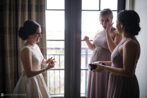Three bridesmaids looking at each other in front of a window during a wedding at the Alfond Inn.