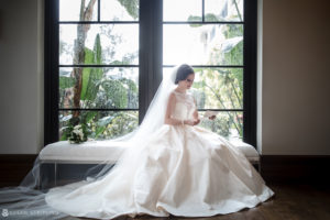 A bride sits in her wedding gown on a bench in front of a window at the Alfond Inn.