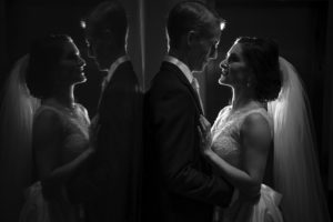 A bride and groom elegantly standing in front of a mirror at their enchanting Alfond Inn wedding.