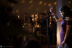 At a Winter Wedding, a woman elegantly holds a glass of wine in front of a group of people at the Front and Palmer venue.