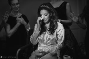In the elegant setting of Philly's Union League, a tearful bride in a robe stands emotionally before her bridesmaids on her wedding day.
