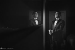 A man in a tuxedo is standing in front of a mirror, preparing for his wedding at Philly's Union League.