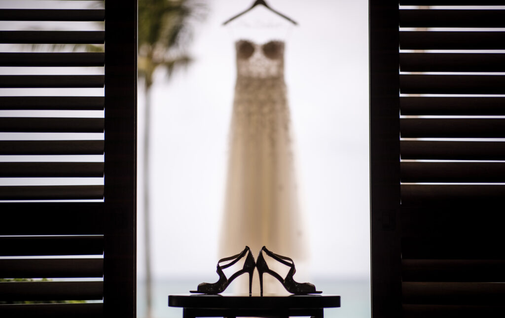 A wedding dress hangs on a table at the Ocean Club in the Bahamas next to a pair of high heeled shoes.