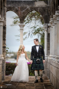 A bride and groom in kilts walking through an archway at their Bahamas wedding.