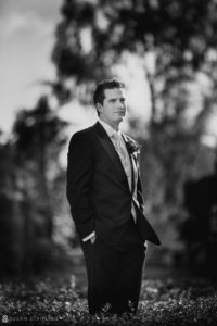 A black and white photo of a groom in a tuxedo at a wedding.