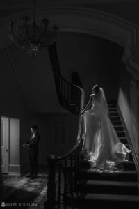 A stunning bride and groom captivate the scene as they stand on the stairs in a dark room, embodying the artistry of a WPPI Grand Master.