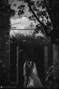 A black and white photo of a wedding couple kissing in front of a gate at Vizcaya during their vow renewal.