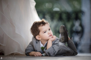 A little boy enchantingly lays on the ground in front of a wedding dress at Vizcaya.
