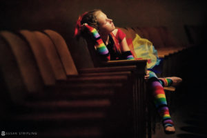 A girl in vibrant stockings sitting on a bench, showcasing her artistry at the WPPI Grand Master level.