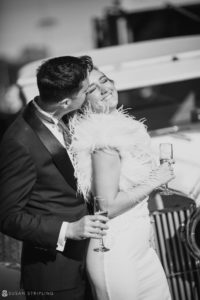 A wedding couple passionately kissing in front of a vintage car at Loews Hotel Philly.