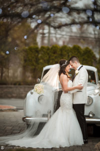 A bride and groom posing next to a classic car at Florentine Gardens estate.