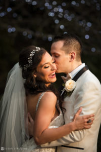 A bride and groom sharing a kiss in front of a Christmas tree at their Florentine Gardens wedding estate.