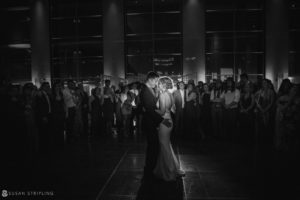 A bride and groom sharing their first dance at a wedding reception in Loews Hotel Philly, surrounded by a large crowd.