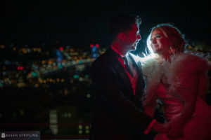 A wedding couple embracing at night in front of the Philadelphia city skyline, outside the Loews Hotel.