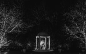 A bride and groom standing in front of a Wedding gazebo at night.