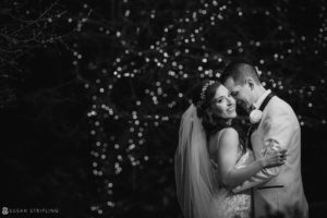 A black and white photo of a bride and groom embracing in front of lights at Florentine Gardens, an exquisite wedding venue estate.
