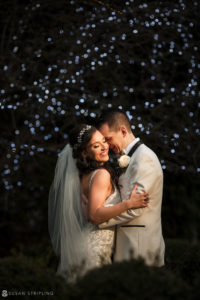 A bride and groom embrace in front of a Christmas tree at their wedding.