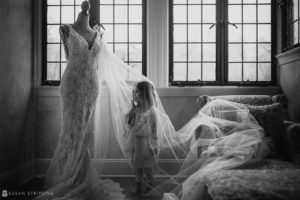 A little girl is standing in front of a window looking at a wedding dress at the Pleasantdale Chateau.