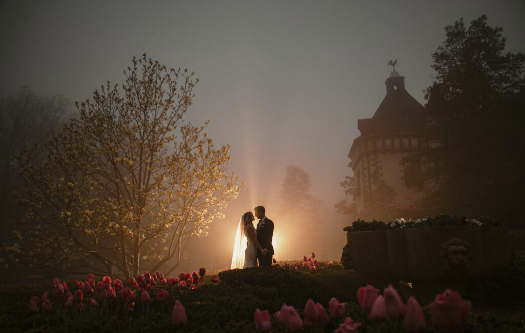 A wedding couple standing in front of tulips at night at Pleasantdale Chateau.
