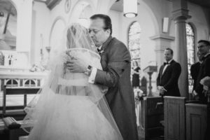A black and white photo of a bride hugging her father at a wedding.