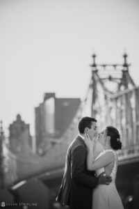 A bride and groom kiss in front of the Brooklyn Bridge on their wedding day.