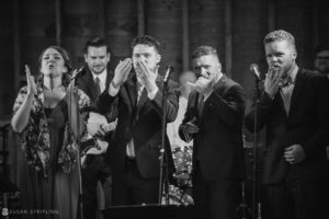 A black and white photo of a group of people singing into microphones at a wedding.