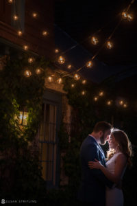 A bride and groom embrace in front of the Stonover Farm house at their wedding celebration, which takes place at night.