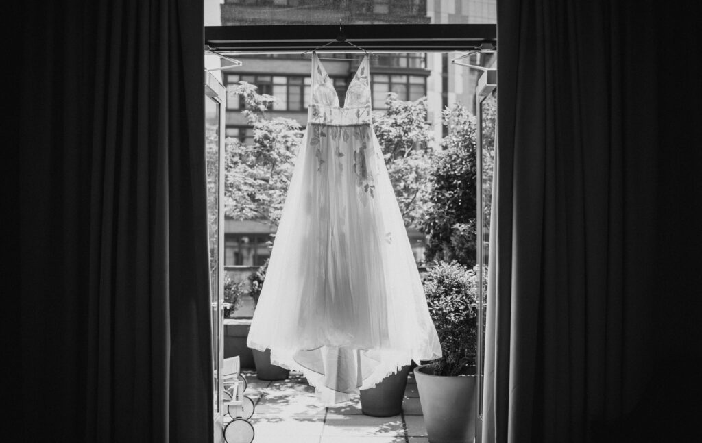 A black and white photo of a wedding dress hanging in a window at the New York Botanical Gardens.