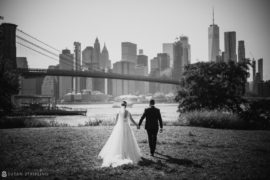 Summer bride and groom walking in front of the Brooklyn Bridge.