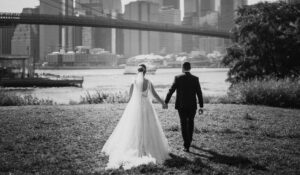 Summer bride and groom walking in front of the Brooklyn Bridge.