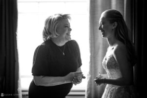 A bride and her mother conversing at the Yale Club, discussing wedding plans in front of a window.