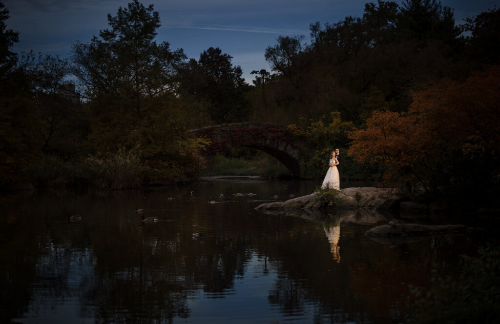 A bride standing on a rock in central park at dusk, capturing the perfect wedding moment amidst the breathtaking scenery.