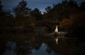A bride standing on a rock in central park at dusk, capturing the perfect wedding moment amidst the breathtaking scenery.